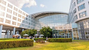 A modern building with a curved glass facade, surrounded by a well-maintained garden with benches and umbrellas. - Van der Valk Hotel Paris CDG Airport (Roissy-en-France)
