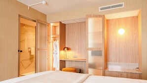 A hotel room with a bed, a walk-in closet, a mirror, and a small table. - Van der Valk Hotel Paris CDG Airport (Roissy-en-France)