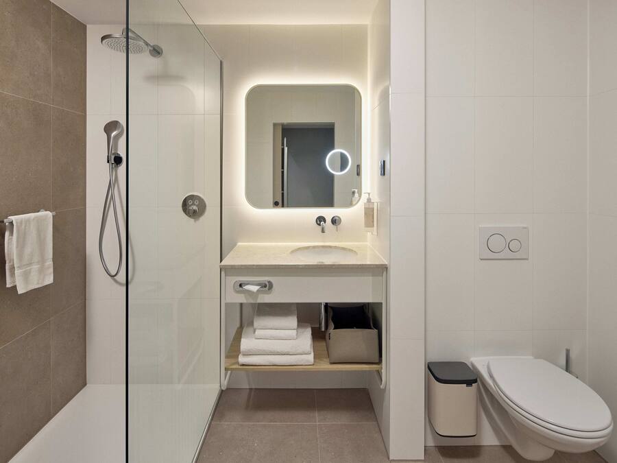 Un baño moderno con ducha envuelta en vidrio, tocador con espejo y un inodoro.