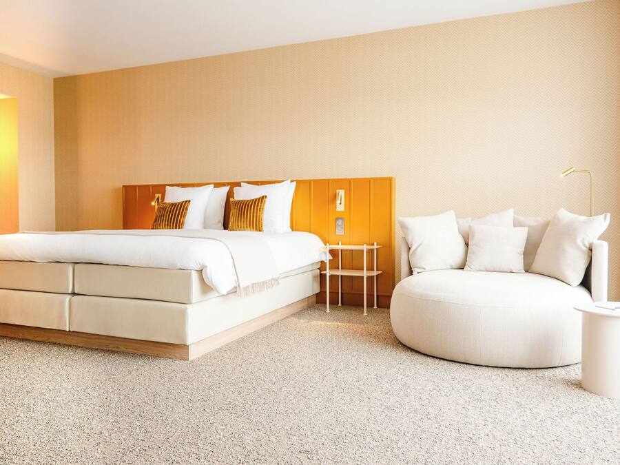 A modern hotel room with a large bed, a round seating area, and a small table.