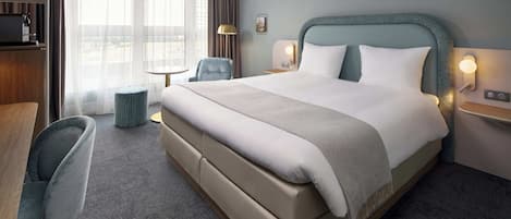 A hotel room with a large bed, a desk, a chair, and a small table.