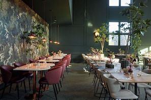 A restaurant with tables and chairs arranged for dining, large windows, and hanging pendant lights.