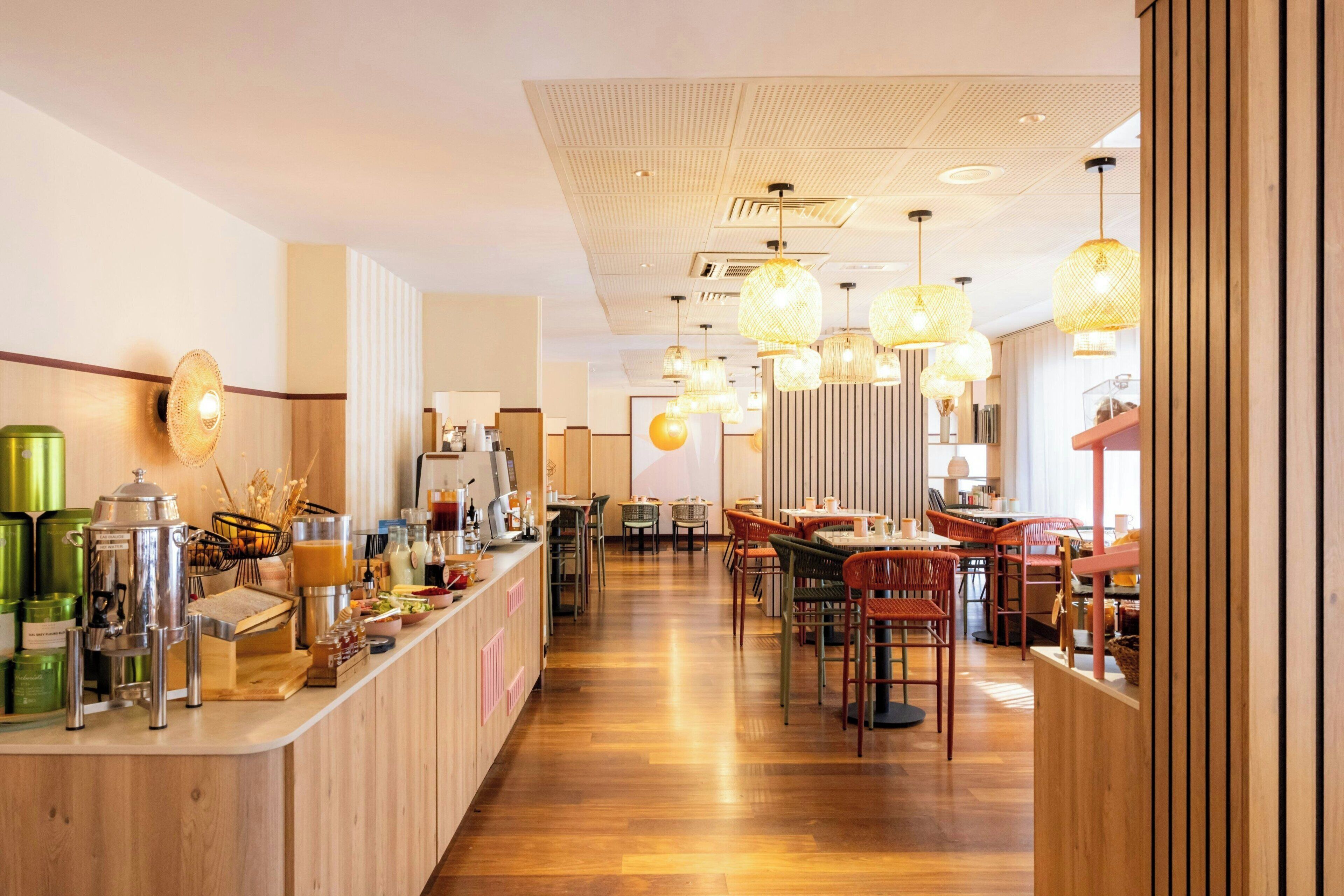 Interior moderno de una cafetería con mostrador de madera, zona de estar e iluminación colgante.