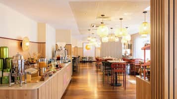 Interior moderno de una cafetería con mostrador de madera, zona de estar e iluminación colgante.