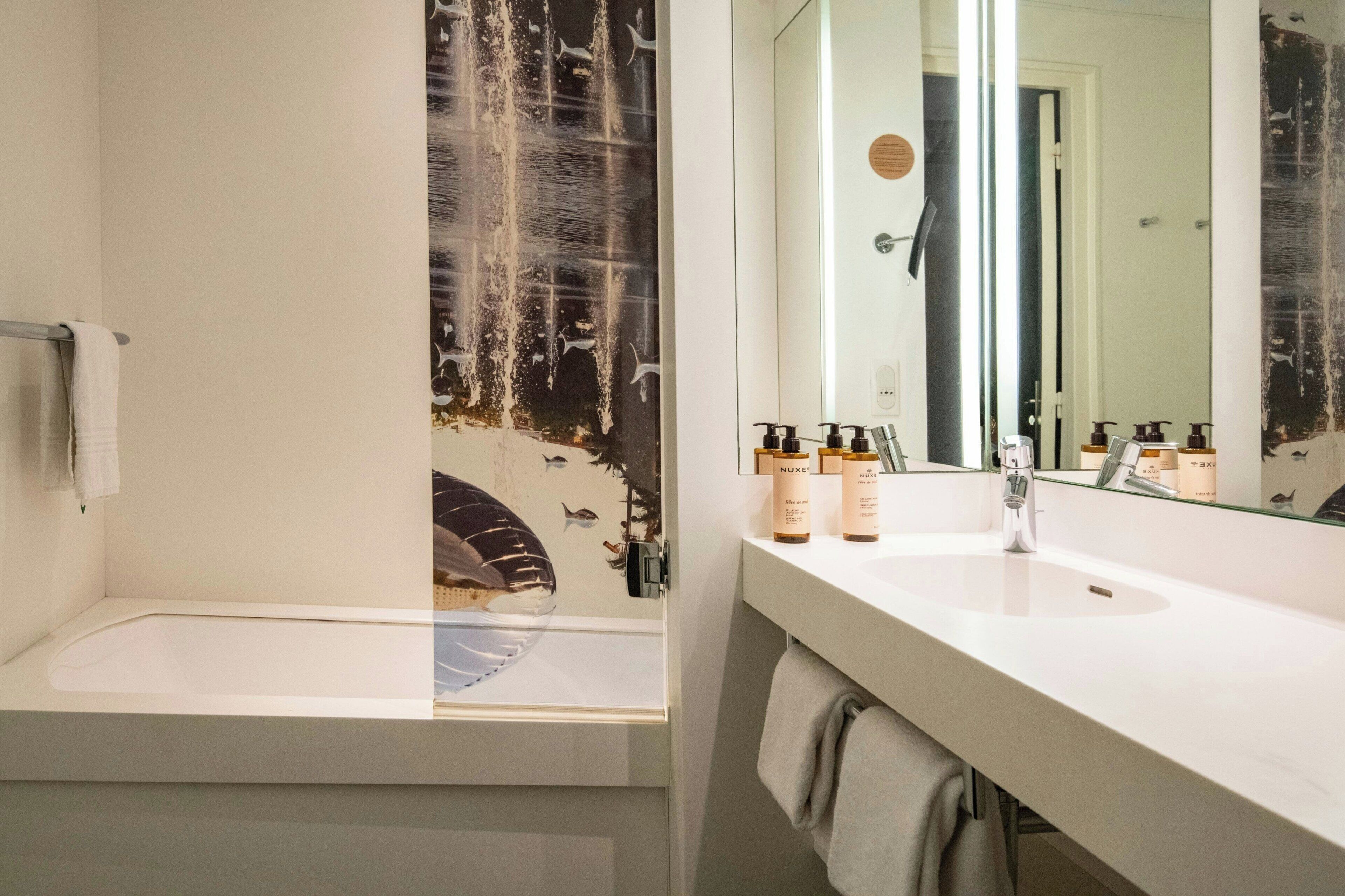 Un baño con bañera, lavamanos con artículos de aseo y un espejo que refleja el cuarto.