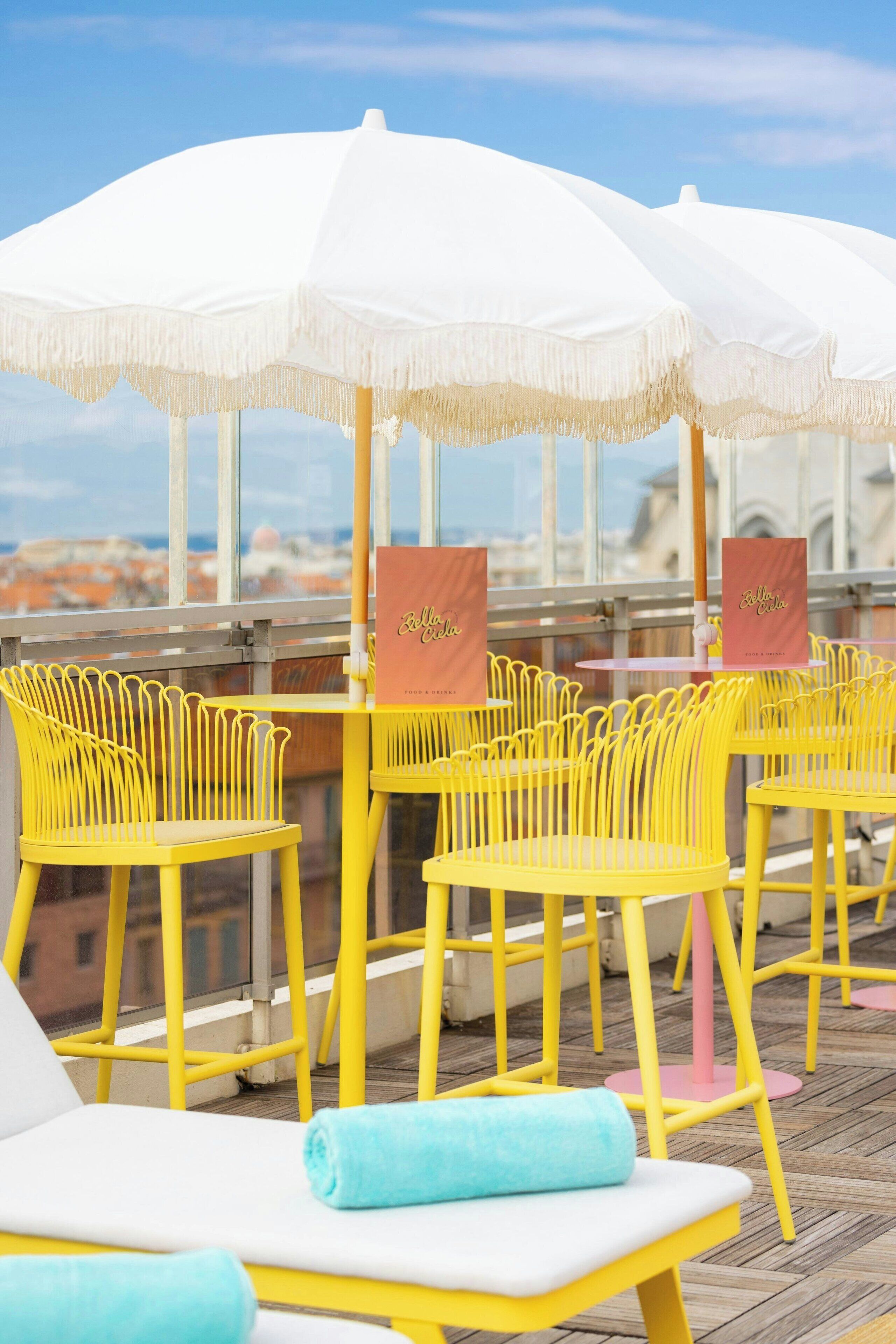 Outdoor seating with yellow chairs and white umbrellas, a view of the cityscape, and a sign for Bella Cala.