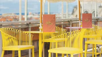 Outdoor seating with yellow chairs and white umbrellas, a view of the cityscape, and a sign for Bella Cala.