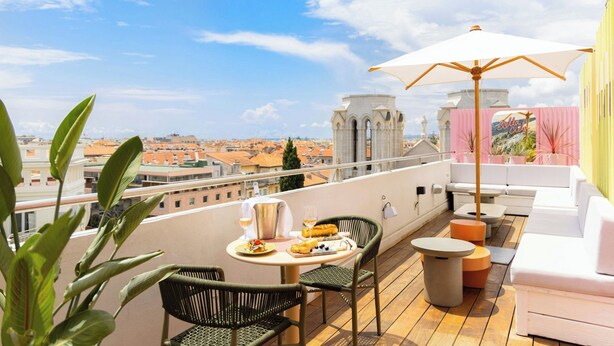 Terraza en la azotea con una mesa preparada para dos personas, una sombrilla blanca y vistas de la ciudad.