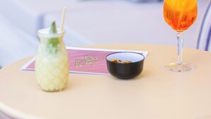 Una mesa redonda con una bebida en un vaso, un cuenco pequeño y una botella sobre un posavasos.