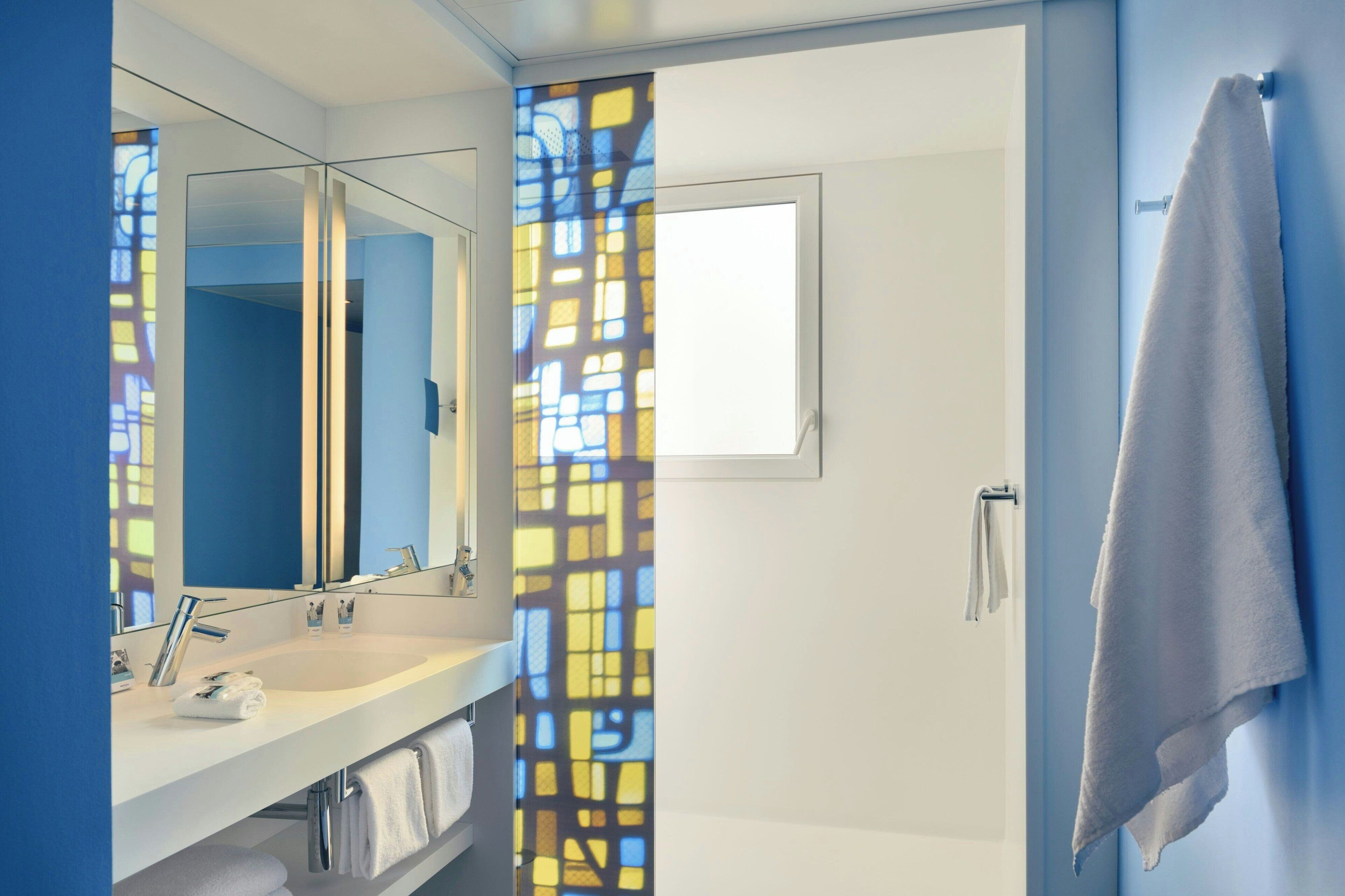 Un baño moderno con un espejo grande, un lavabo blanco y un perchero para toallas.
