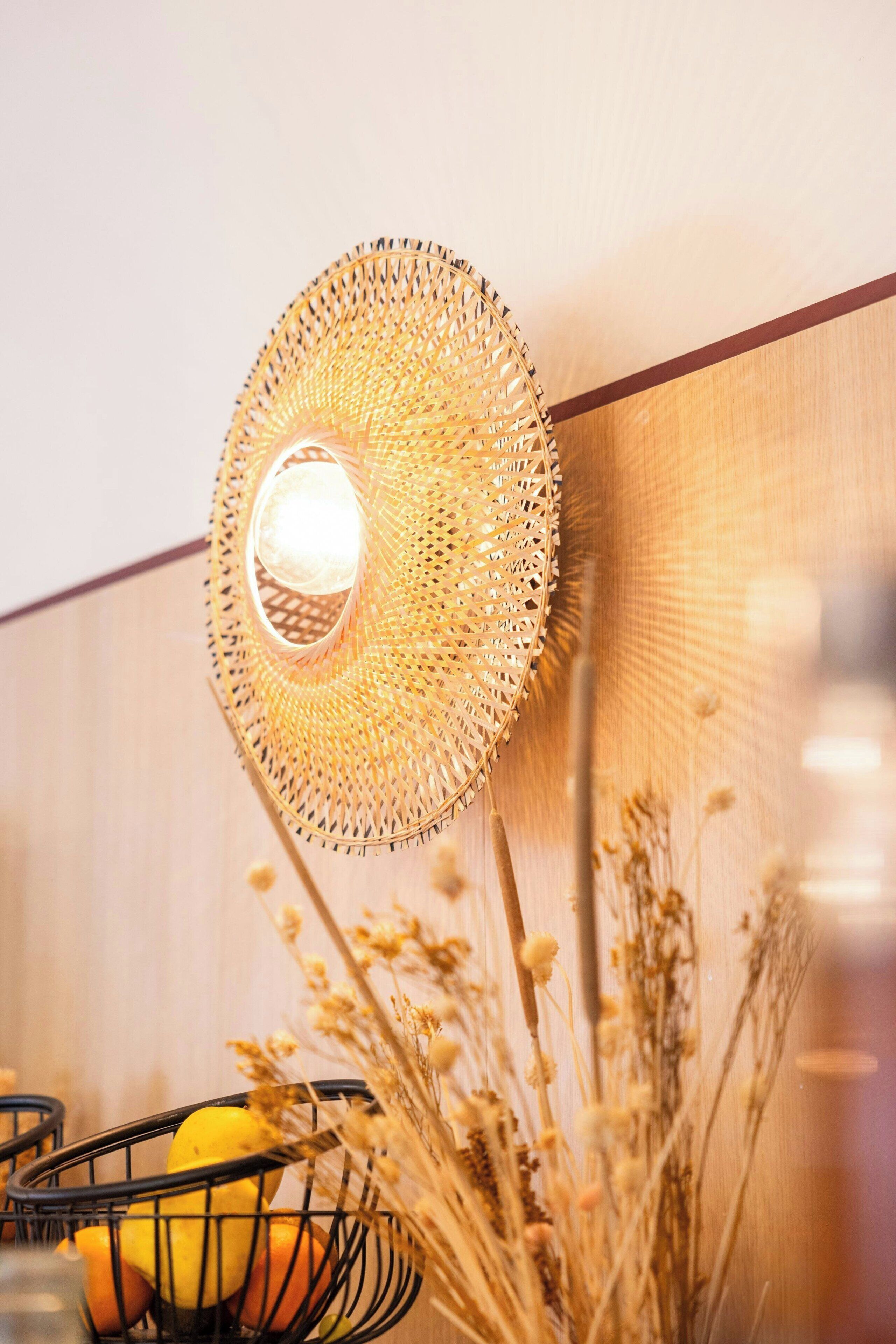 A woven wall hanging with a light fixture, a fruit basket, and dried plants.
