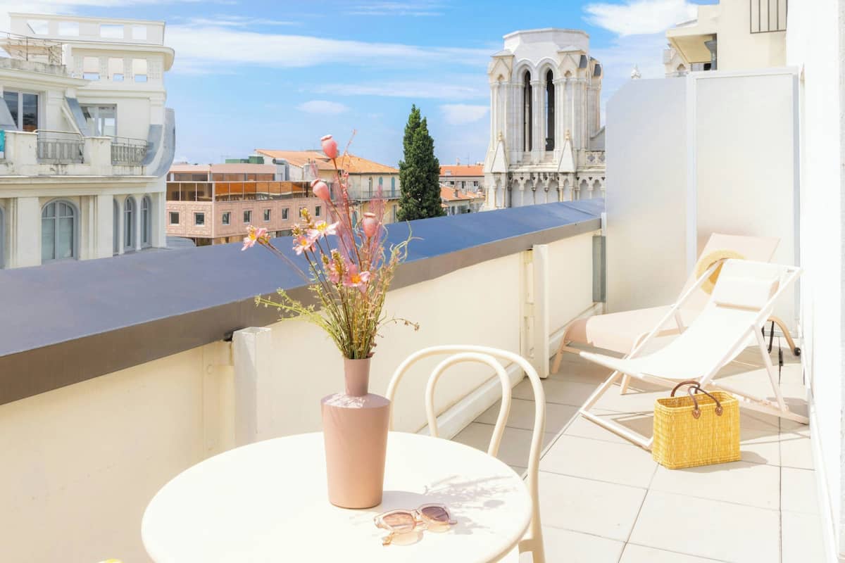 A balcony with a table, chairs, a vase with flowers, and a view of buildings and a church.
