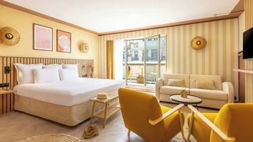 Una habitación de hotel con una cama grande, un sofá, dos sillones amarillos, una mesita y un televisor.