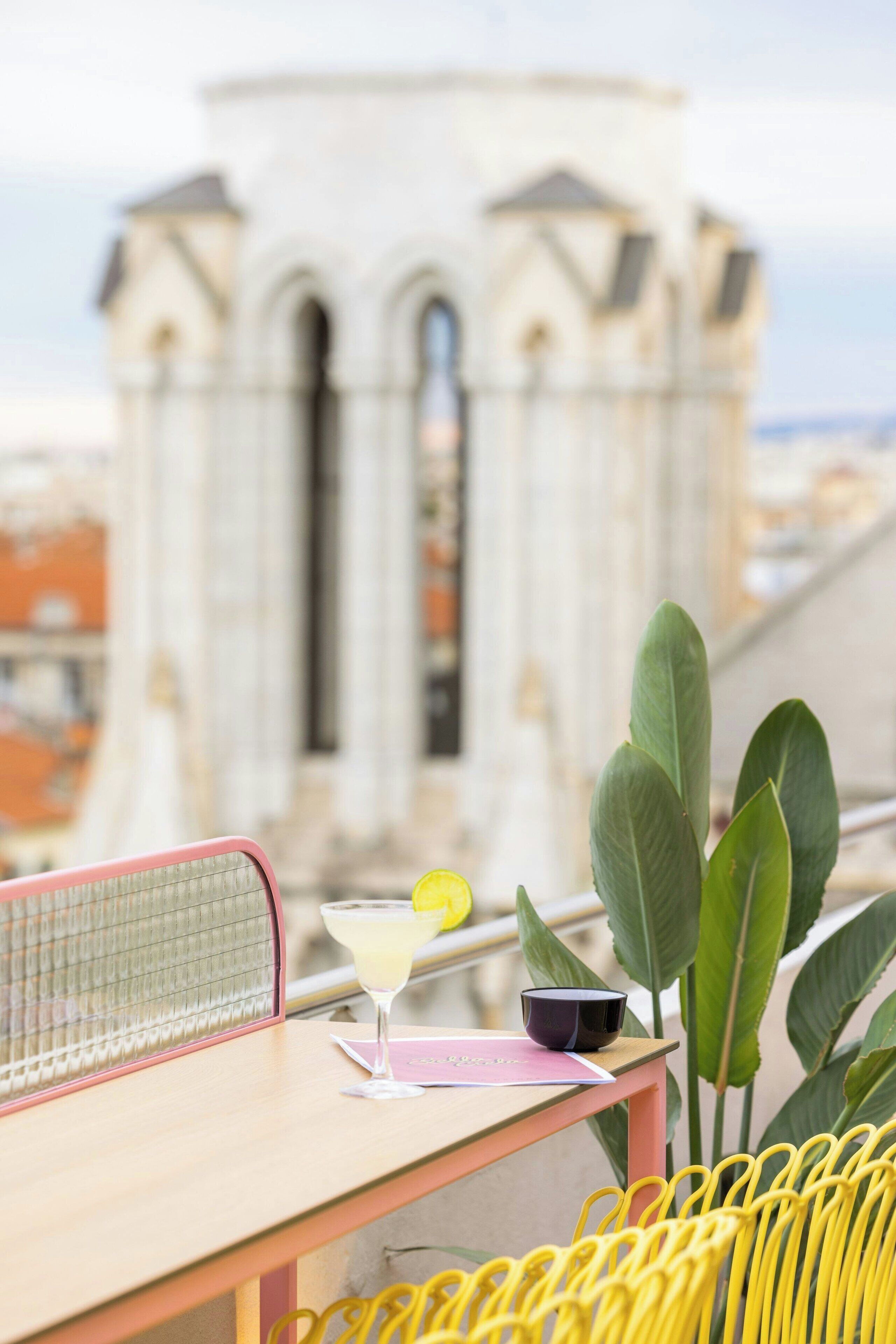 A table with a drink, a bowl, and a menu, set against a backdrop of a building with arches.