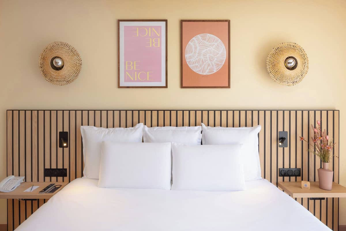 A neatly made bed with white linens, a wooden headboard, and two wall-mounted light fixtures.