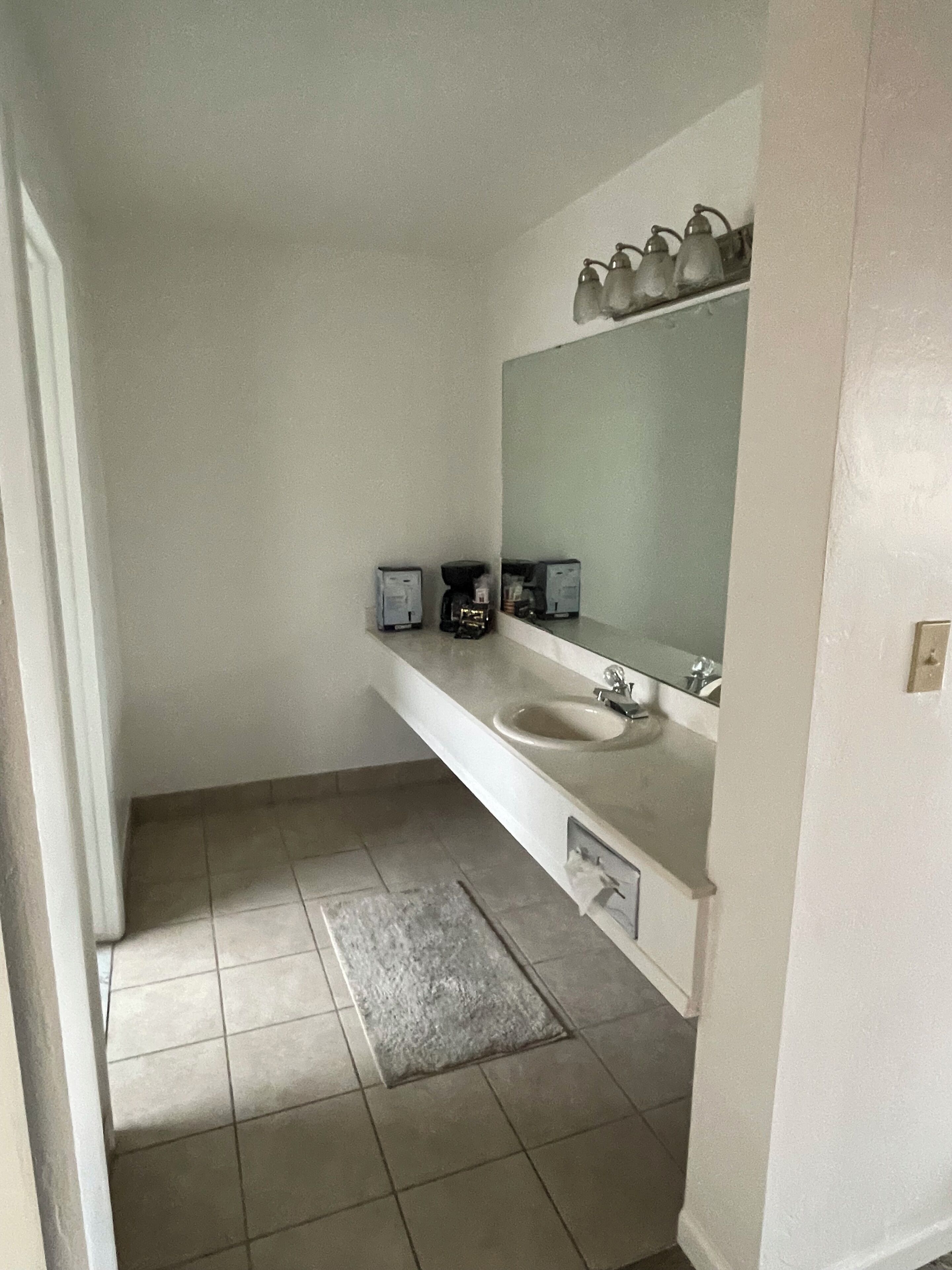 A bathroom with a white sink, a mirror, and a coffee maker on the countertop.