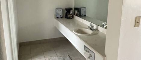 A bathroom with a white sink, a mirror, and a coffee maker on the countertop.