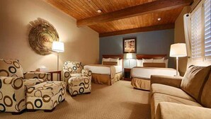 A hotel room with a wooden ceiling, two beds, a sofa, and patterned armchairs.