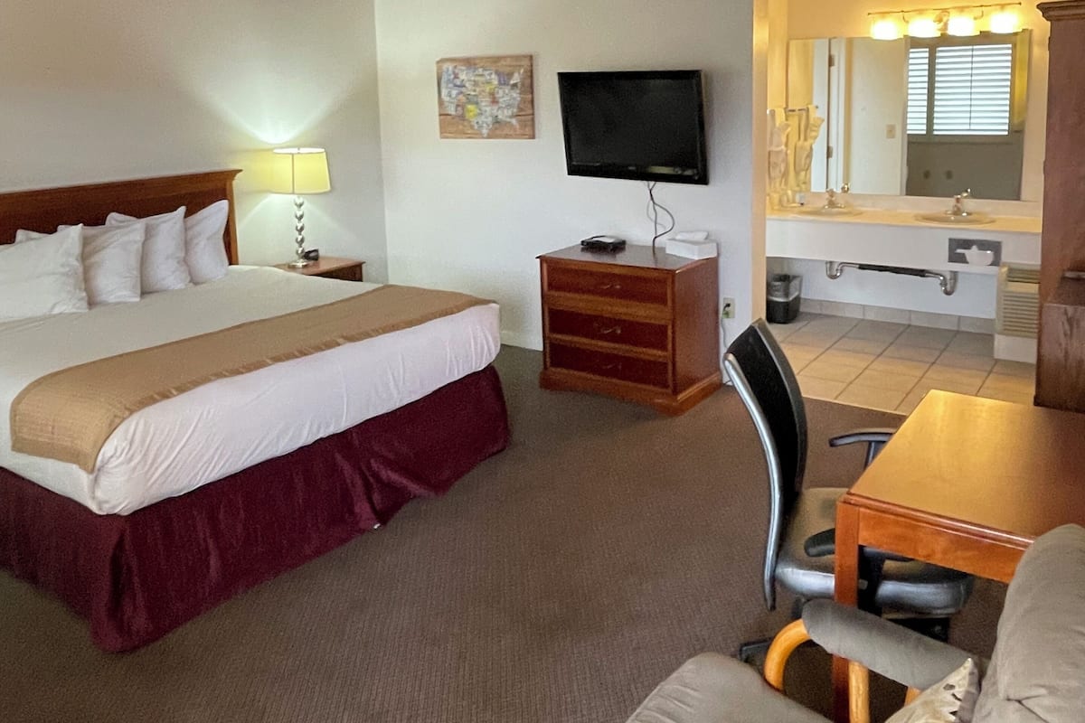 Une chambre d’hôtel avec un lit, une télévision, un bureau, une chaise et une salle de bain visible à travers une porte ouverte.