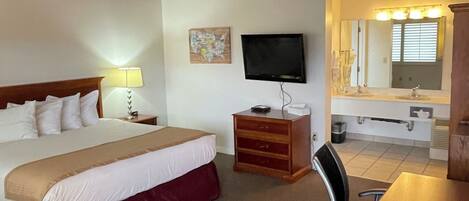 A hotel room with a bed, a TV, a desk, a chair, and a bathroom visible through an open door.
