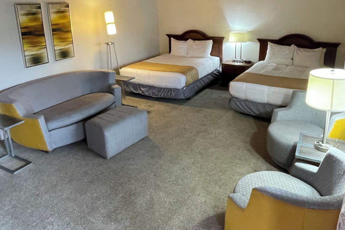 Une chambre d’hôtel avec un canapé, deux lits simples, une petite table et une lampe.