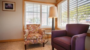 A room with a floral armchair, a purple armchair, and a lamp near a window with blinds.