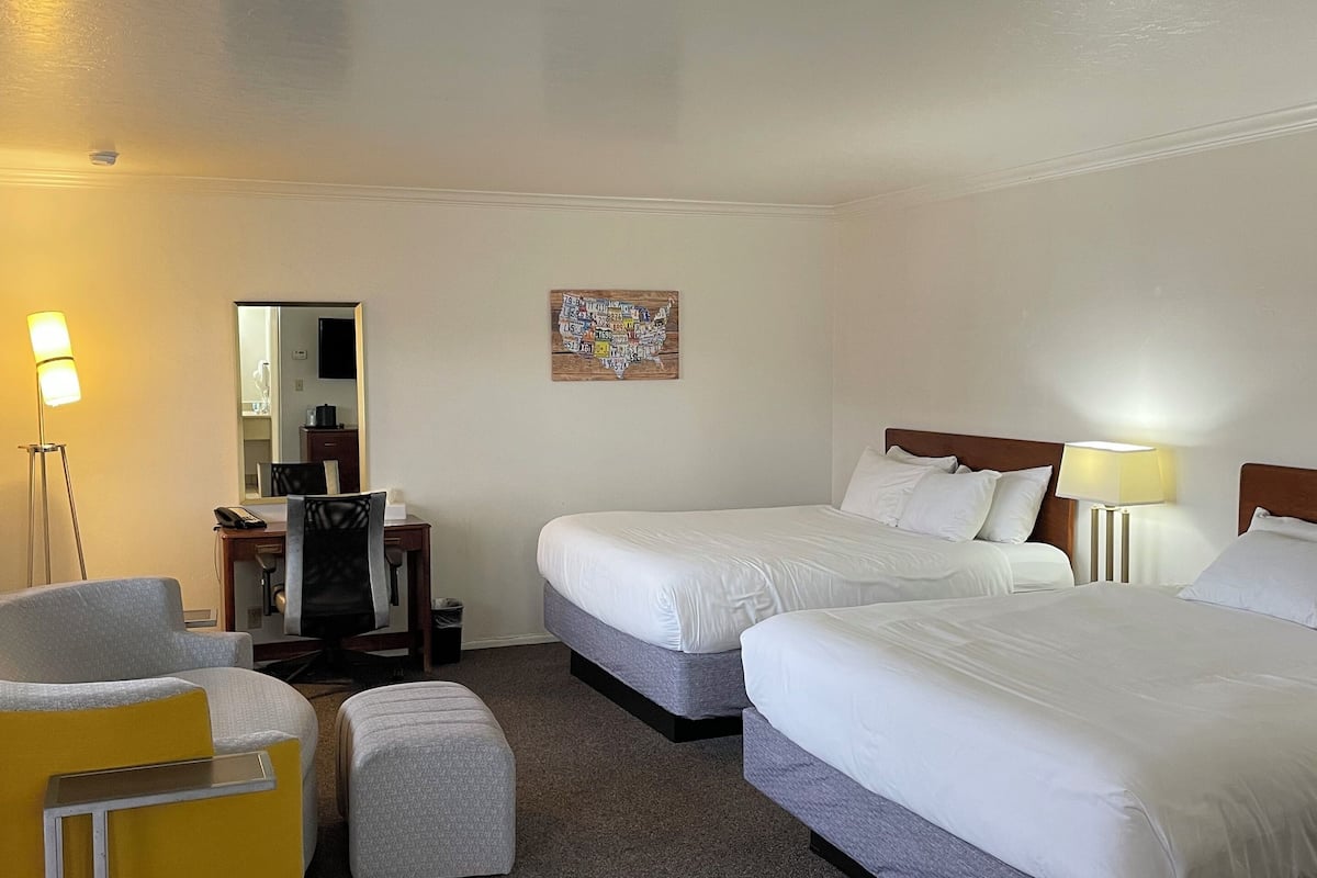 Une chambre d’hôtel avec deux lits, un bureau, une chaise et une petite table.