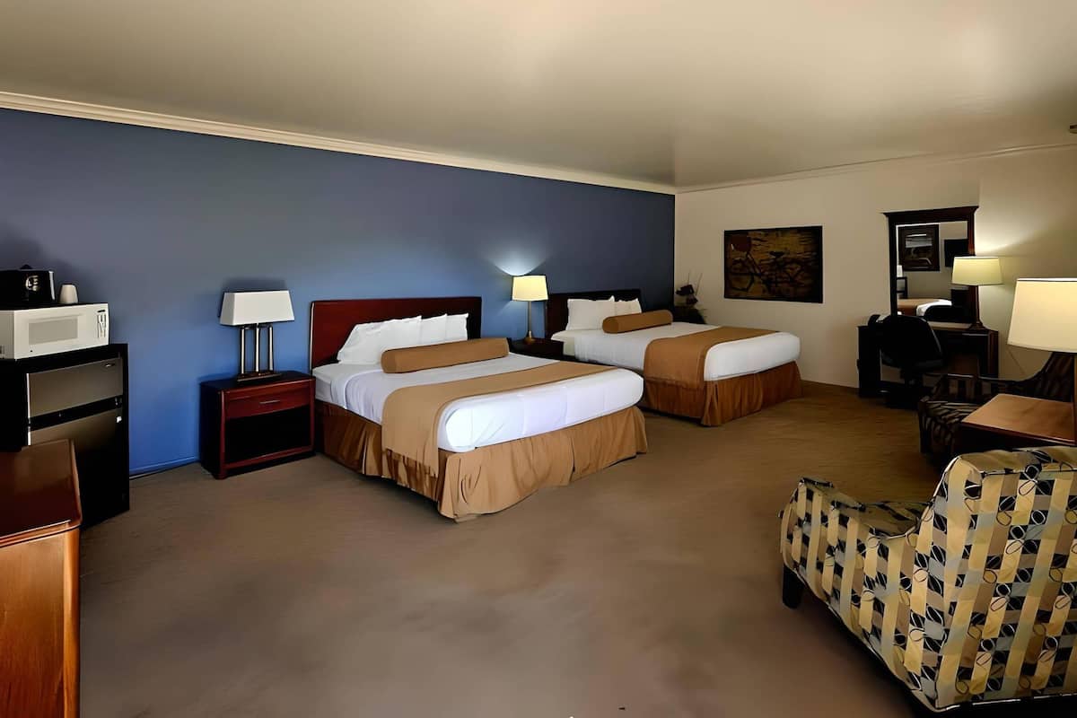 Une chambre d’hôtel avec deux lits, un bureau, une chaise, un four à micro-ondes et une lampe.