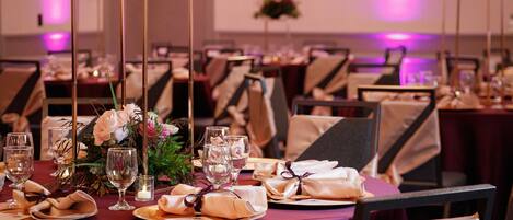 A banquet hall with round tables set for a formal event, featuring floral centerpieces and neatly arranged table settings.