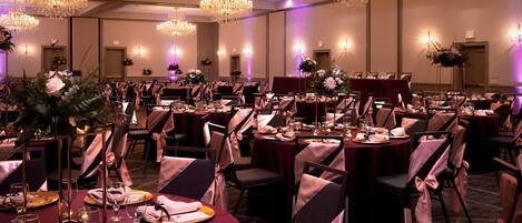 A banquet hall with round tables, chairs, and chandeliers.