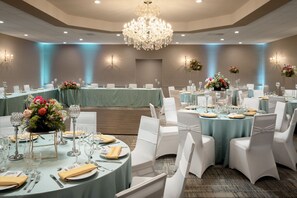 Una sala banchetti con tavoli rotondi, sedie bianche e centrotavola floreali.