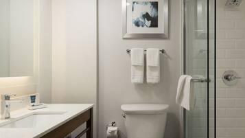 Un baño moderno con un lavabo blanco, una cabina de ducha de vidrio y un cuadro abstracto enmarcado sobre el inodoro.