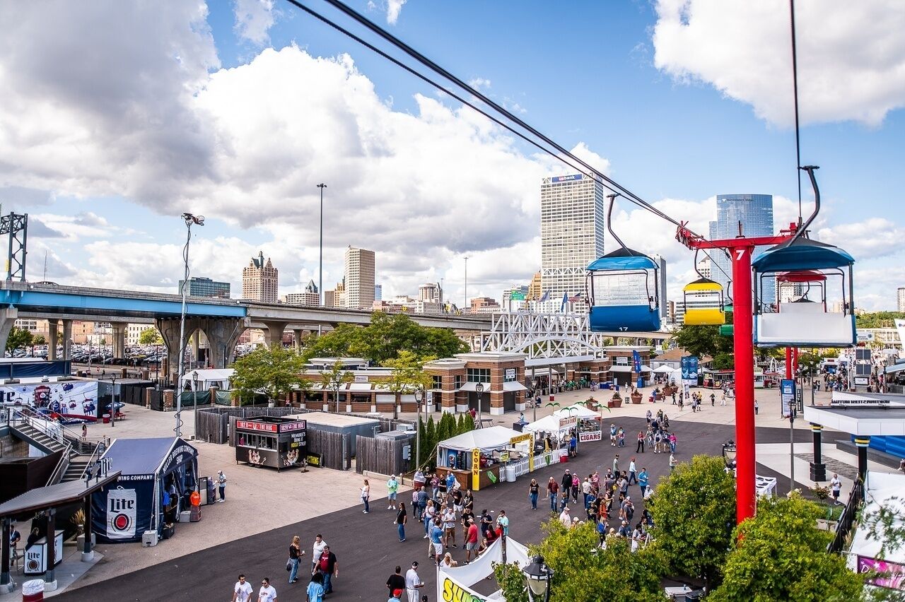 A bustling urban square with a tram system, a prominent red pole, and various commercial stalls.