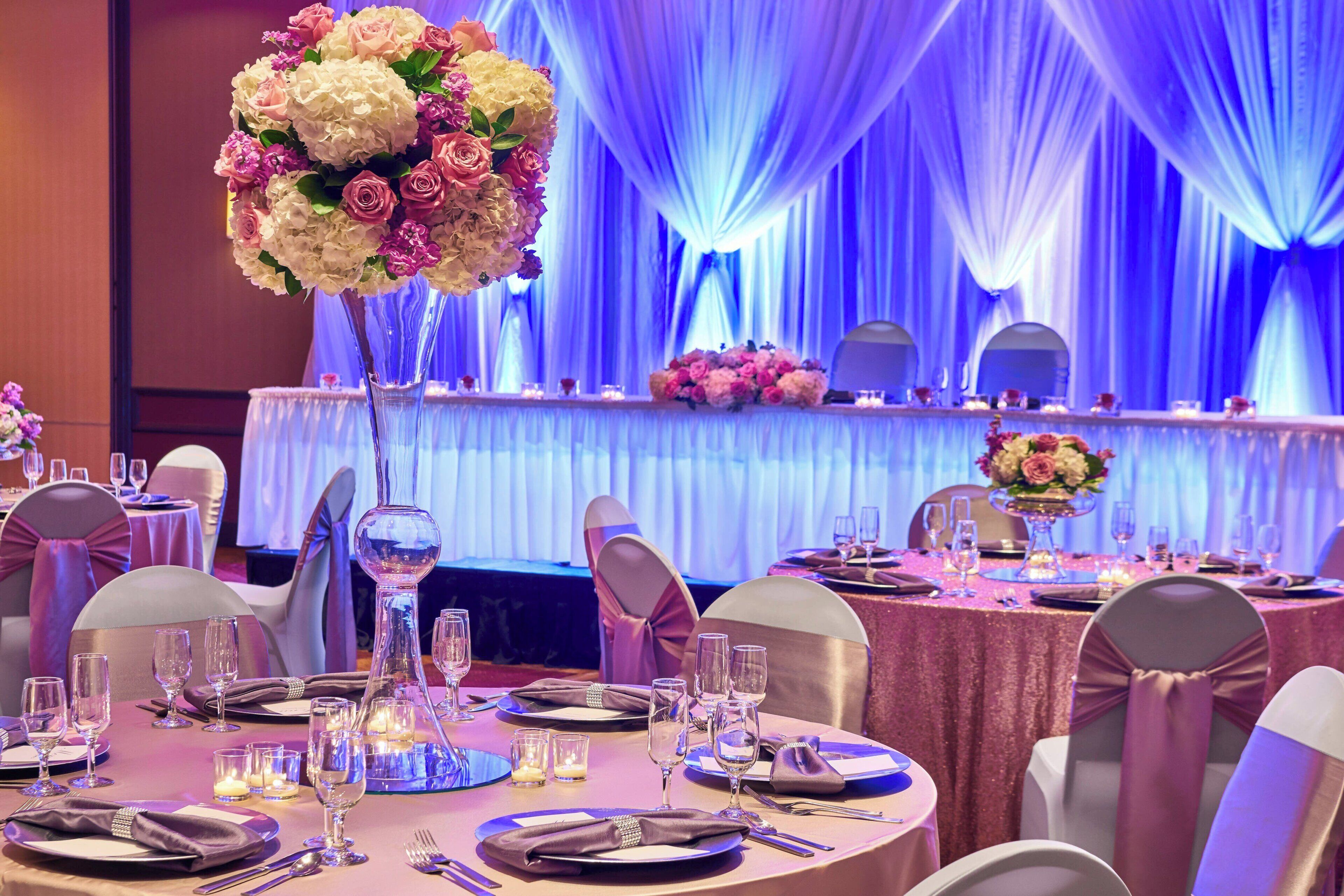 A banquet hall with round tables set for a formal event, featuring floral centerpieces and elegant table settings.