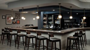 A bar area with a long counter, multiple stools, and hanging pendant lights. - Four Points by Sheraton Milwaukee North Shore (Milwaukee)