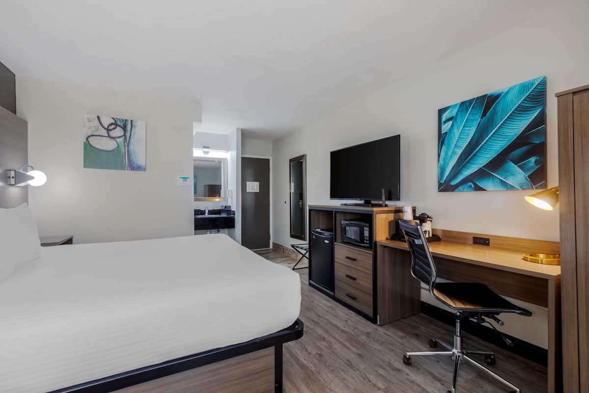 Quarto de hotel moderno com cama, escrivaninha, cadeira, TV e obras de arte.