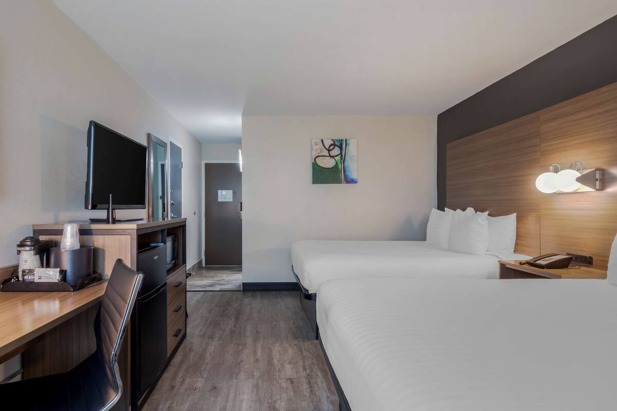 Quarto de hotel com cama, escrivaninha com computador, televisão e máquina de café.