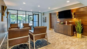 A modern hotel lobby with leather sofas, a wooden reception desk, a flat-screen TV, and a large window offering a view of the outdoors. - Best Western Corpus Christi Airport Hotel (Corpus Christi)