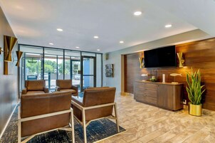 Een moderne hotellobby met leren banken, een houten receptiebalie, een flatscreen televisie en een groot raam met uitzicht op het omliggende landschap.