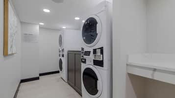 Une buanderie équipée de plusieurs machines à laver et de plusieurs sèche-linge, un mur blanc avec un panneau et un plancher en bois.