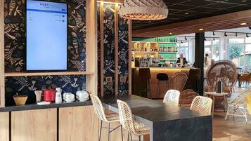 Un espace bar avec un comptoir en bois, des chaises en osier et un grand écran affichant le menu.