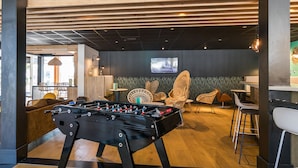 Un espacio interior moderno con mesa de fútbol, sillas de mimbre y una zona de bar.