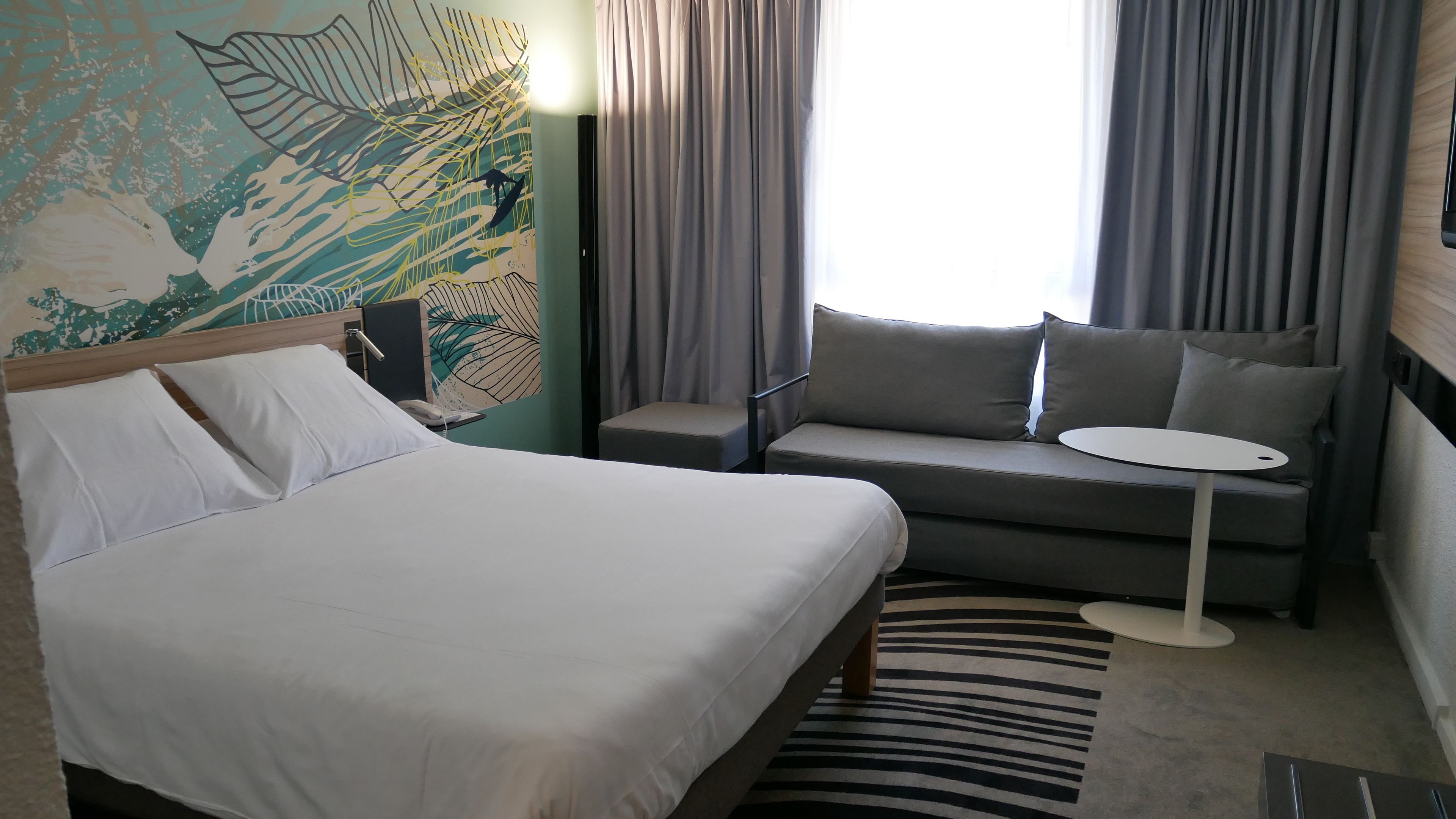 A hotel room with a bed, a sofa, a small table, and a patterned rug.