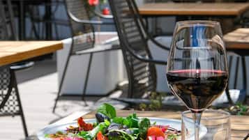 Un comedor al aire libre con una mesa lista para una comida, una copa de vino tinto y un plato de ensalada.