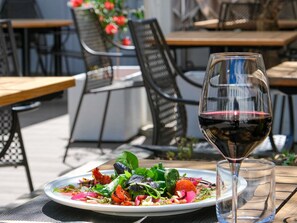 An outdoor dining area with a table set for a meal, a glass of red wine, and a plate of salad.
