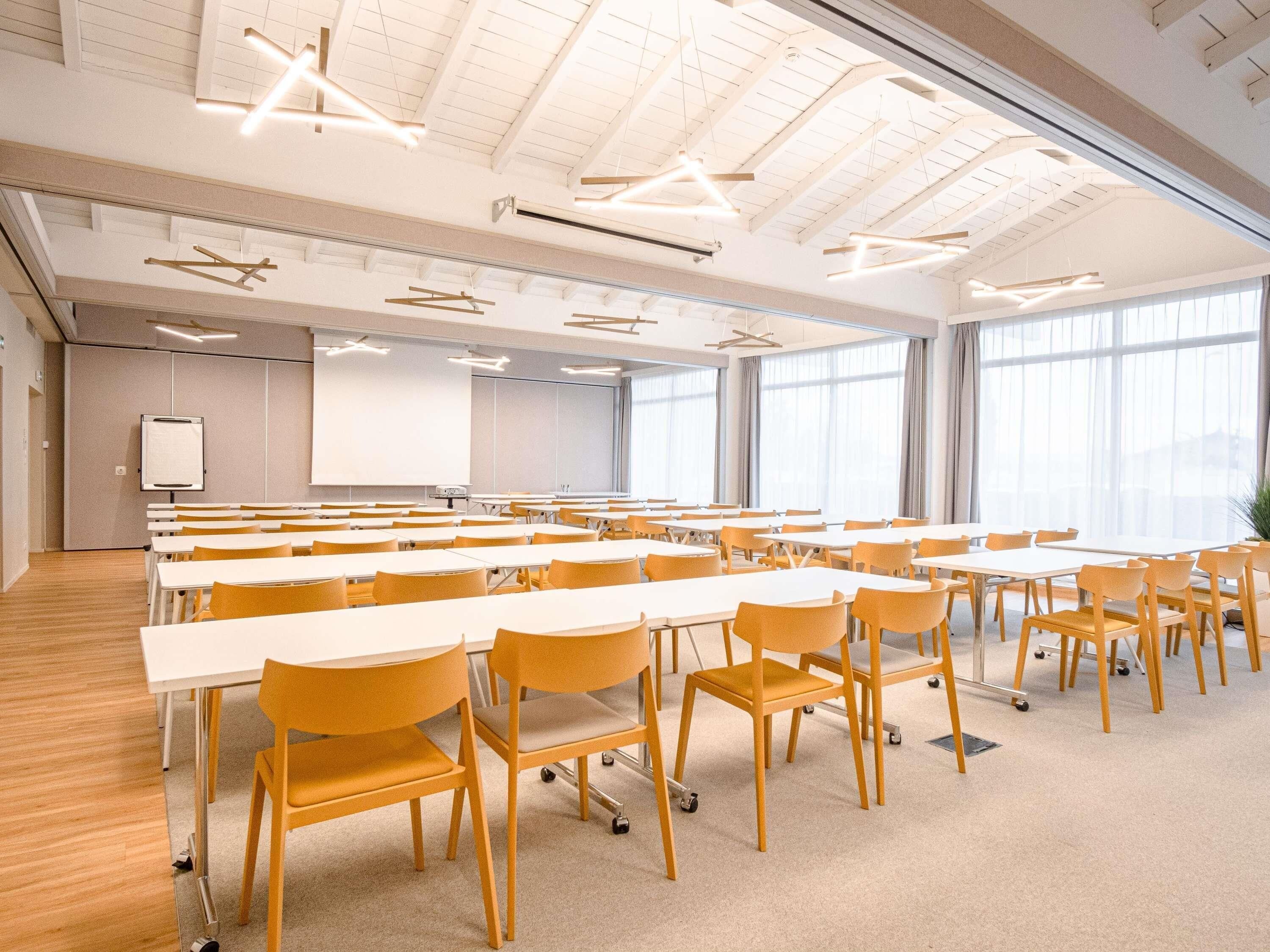 Een vergaderruimte met tafels, stoelen, een whiteboard en grote ramen.