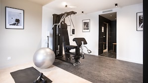 Un gimnasio en casa con una bicicleta estática, una pelota de ejercicios grande y mancuernas. Hay cuadros en las paredes y una puerta que da a otra habitación.