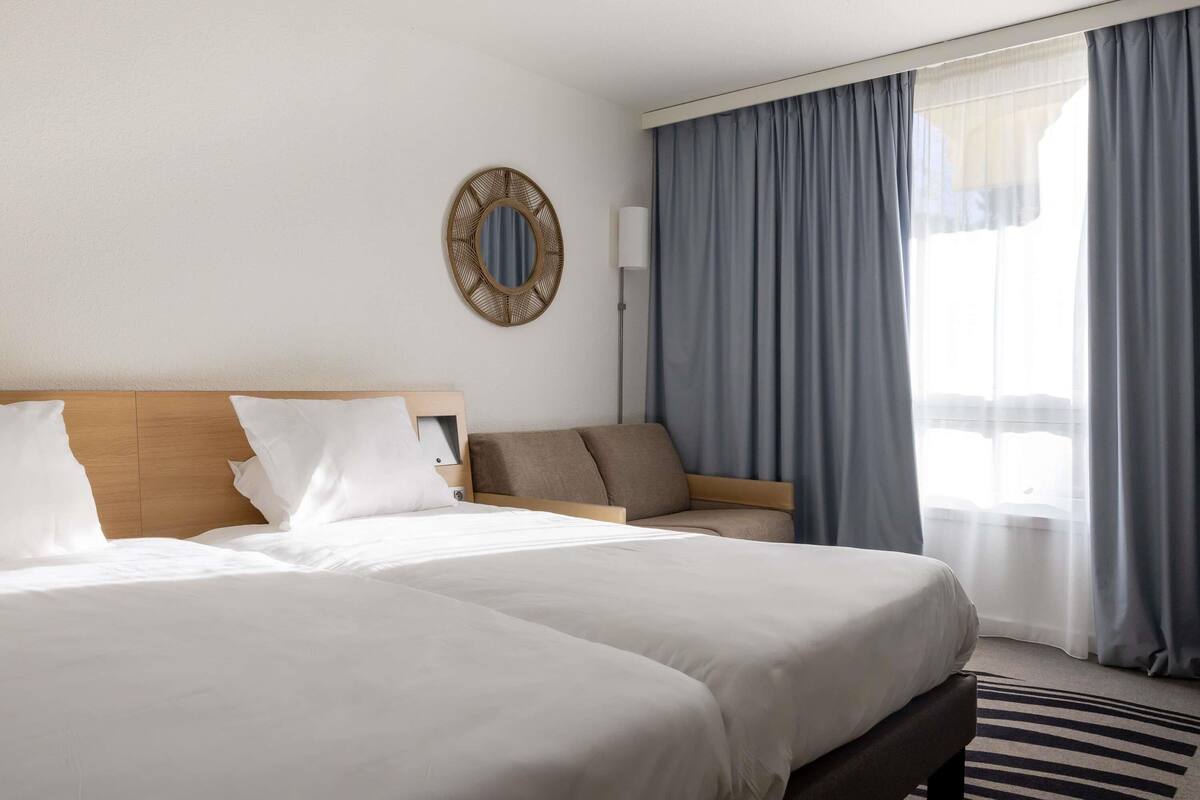 A hotel room with a large bed, a sofa, a mirror, and a view of the outdoors.