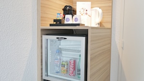 Un refrigerador compacto con puerta de vidrio, que contiene bebidas y una botella de Evian.