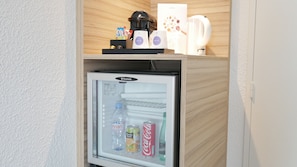 Un refrigerador compacto con puerta de vidrio, que contiene bebidas y una botella de Evian.